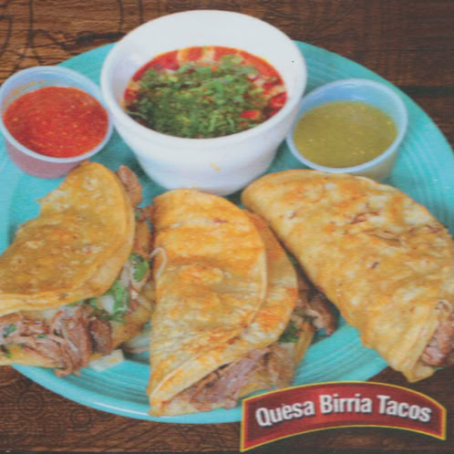 Close-up of assorted Mexican tacos with fresh vegetables, herbs, and vibrant garnishes on a wooden table.